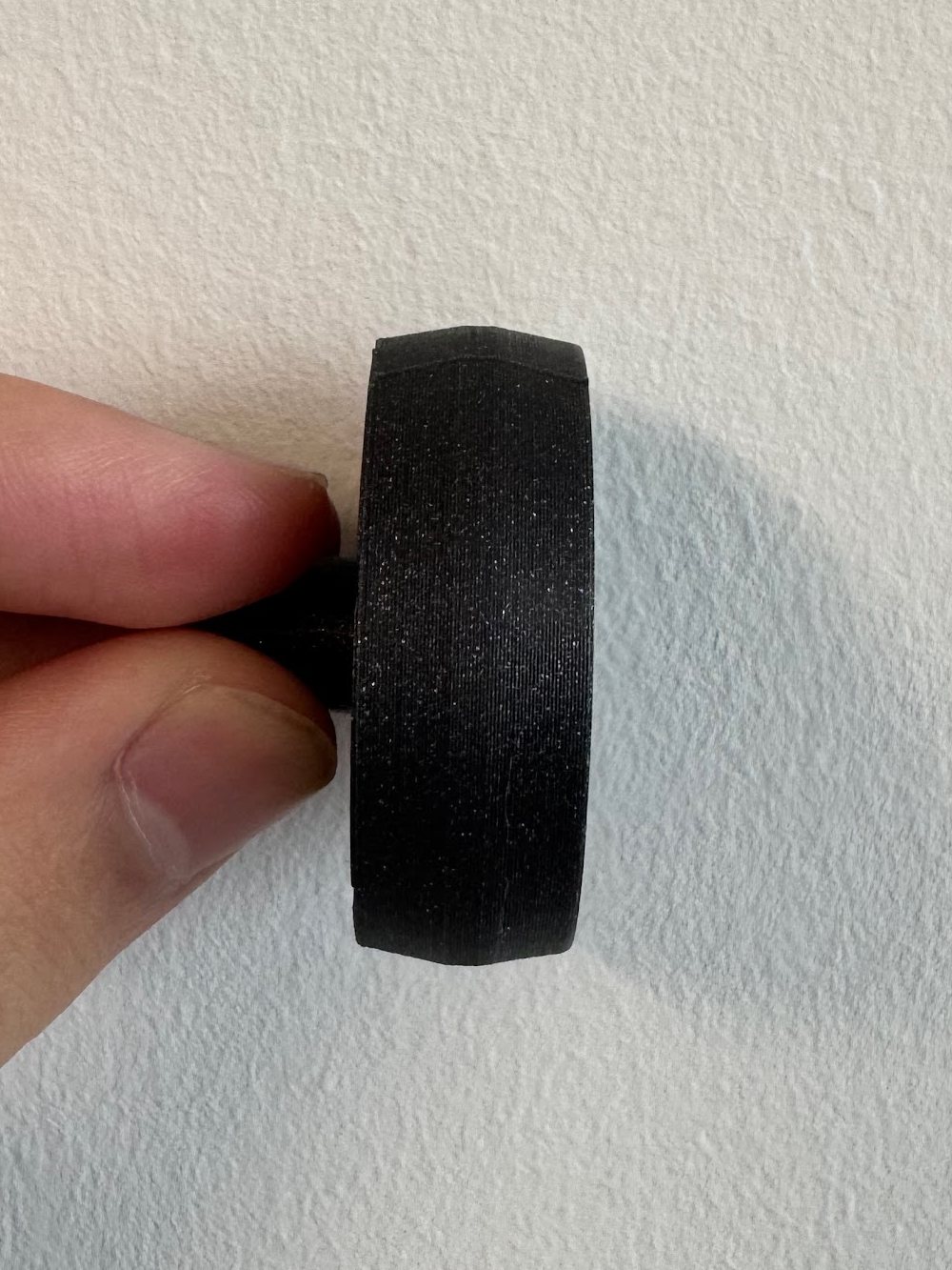 A reprinted black wheel held edge-on against a white wall, showing its convex face