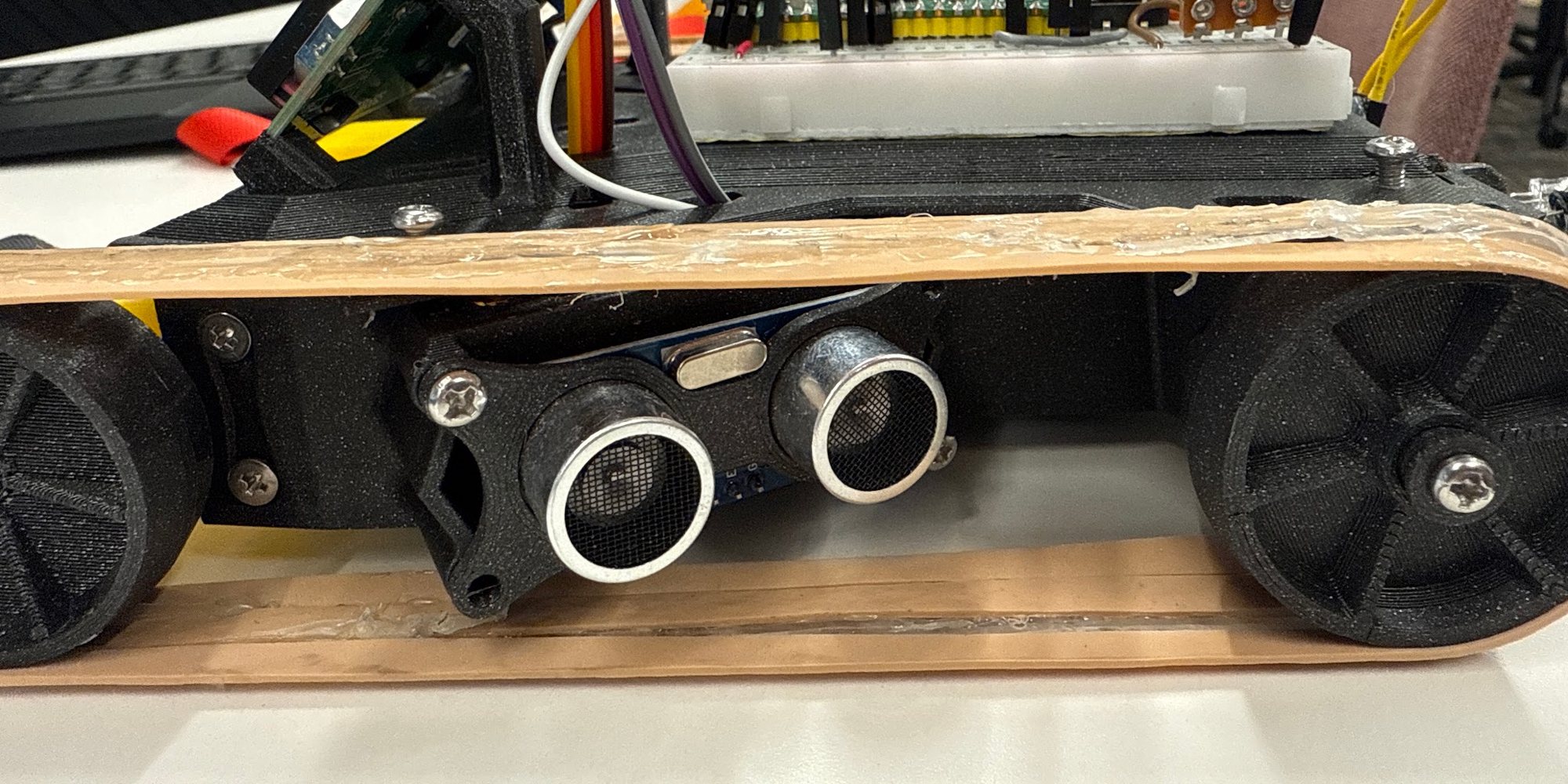 Side view of the maze robot: an ultrasonic sensor sits recessed between the two runs of a rubber-band tread, with the Pico, breadboard, potentiometer and LED strip on top