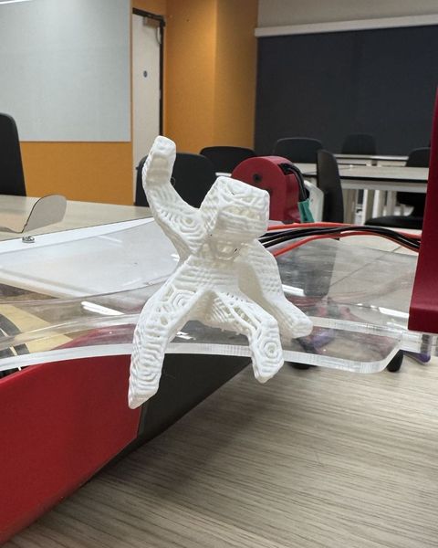 A white 3D-printed figure of Grace from Project Hail Mary sitting on V1's clear acrylic deck