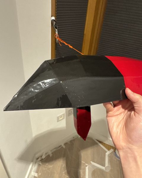 A printed V1 hull section held up after its epoxy coat, black at the bow and red behind