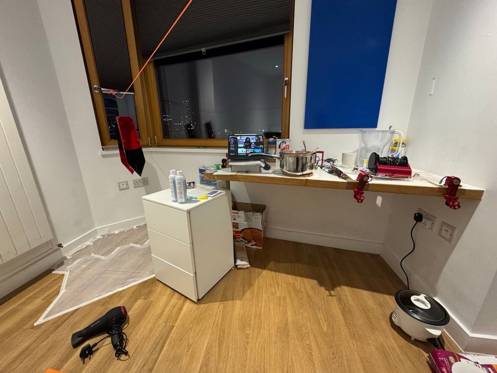 Our room in London set up as a workshop: a hull section hanging over a taped-down drop sheet, the winch and wiring on the desk